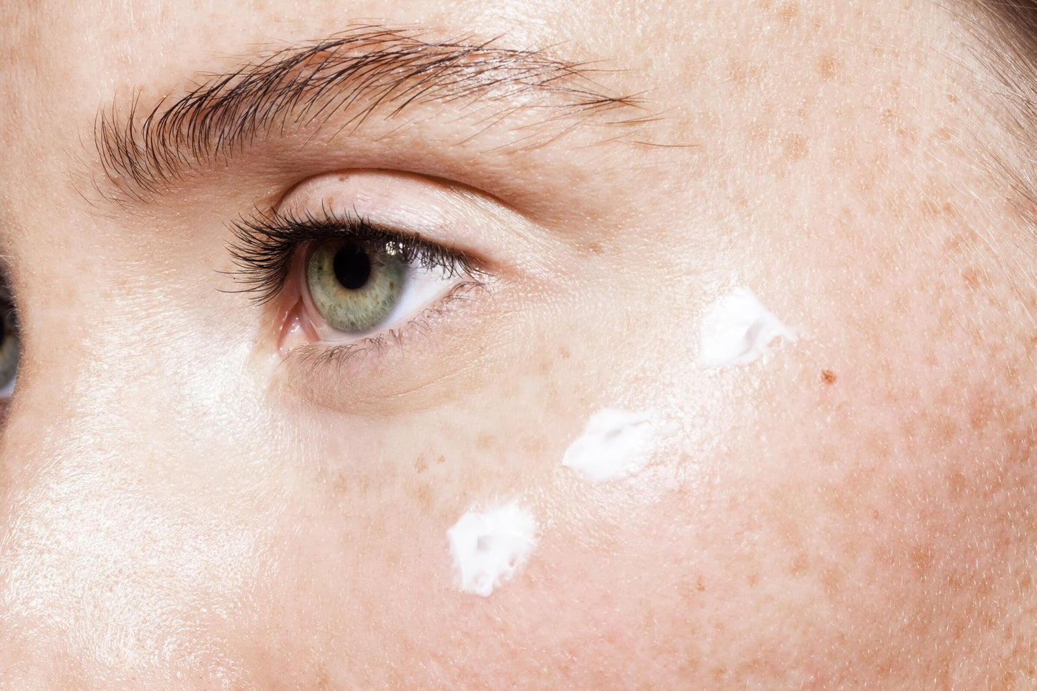 Close-up of a green eye with white cream swatched on cheek, emphasizing skin barrier repair and care