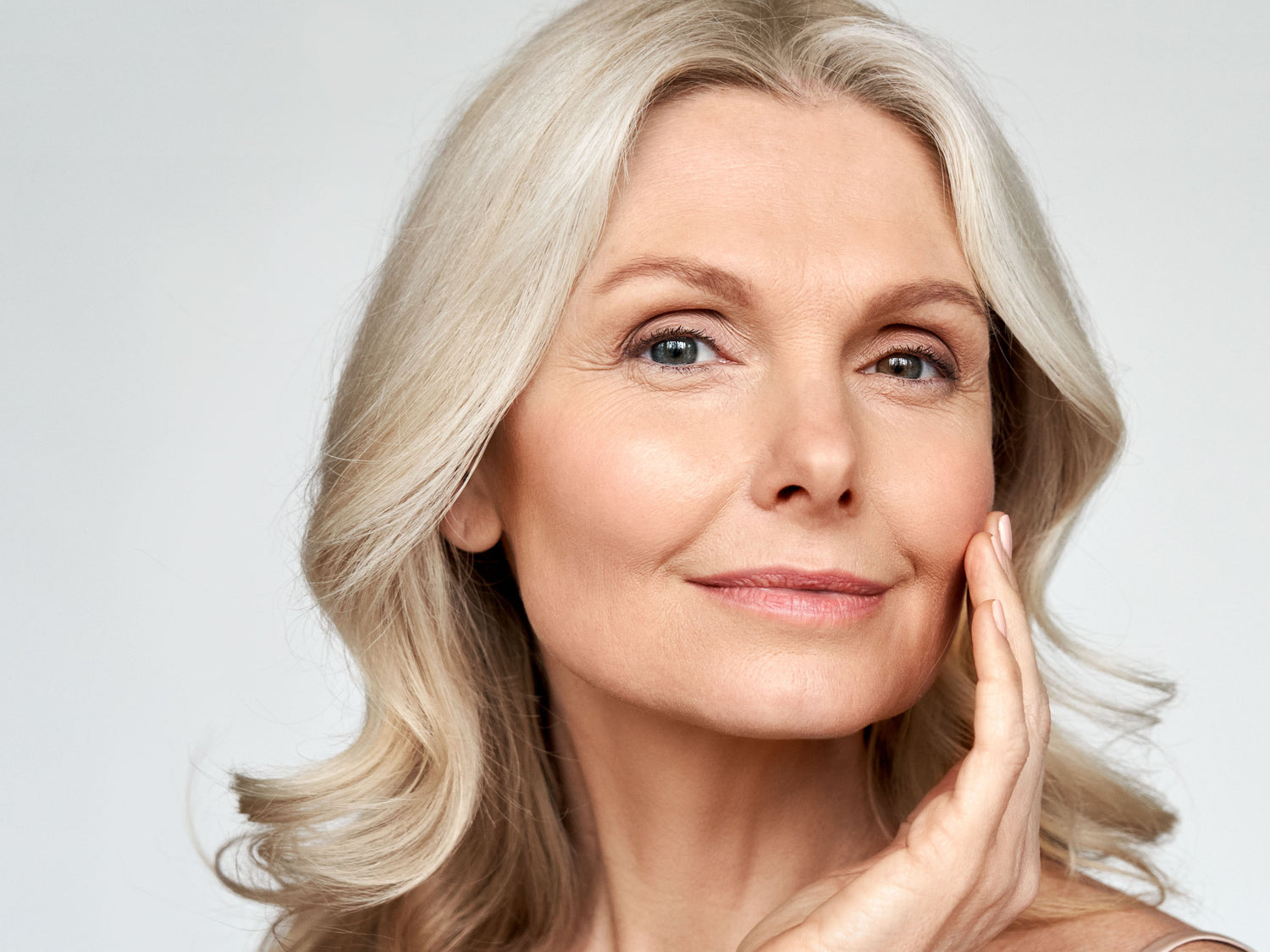 A smiling mature woman touching her face, showcasing radiant, healthy skin