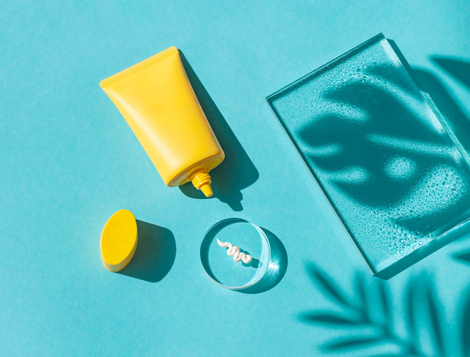 Yellow sunscreen tube with a product swatch on a glass against a blue background with shadows, featuring a No-BS guide to sunscreen