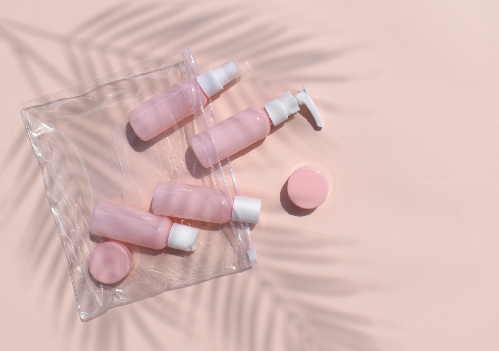 Flat lay of travel-sized pink skincare bottles on a peach background, featuring an article about Dr. Shereene Idriss’ in-flight skincare routine