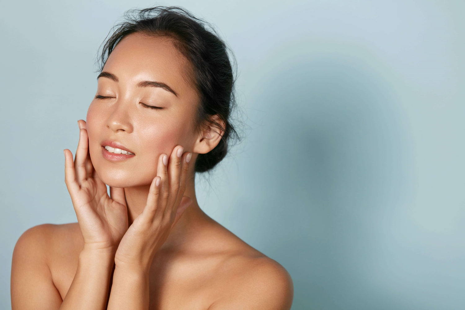 Woman with radiant, tawny, skin against a blue background, exemplifying proper acne prevention techniques