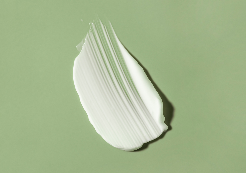 Close-up of a white cream swatch on a green background, highlighting the benefits of Azelaic Acid in skincare