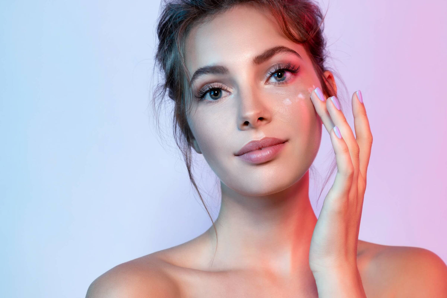 Woman in messy bun applying skincare to her face against a blue background, featuring an article on the correct order of a skincare routine