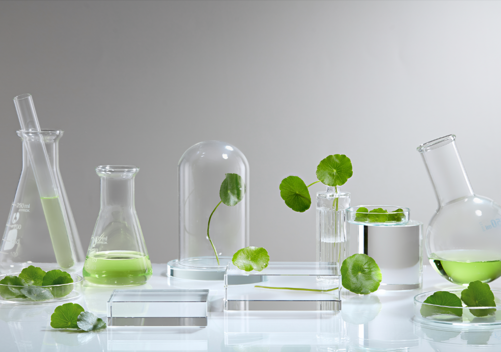 Centella Asiatica leaves with lab beakers and glass jars filled with green liquid, showcasing its skin-soothing, anti-redness properties