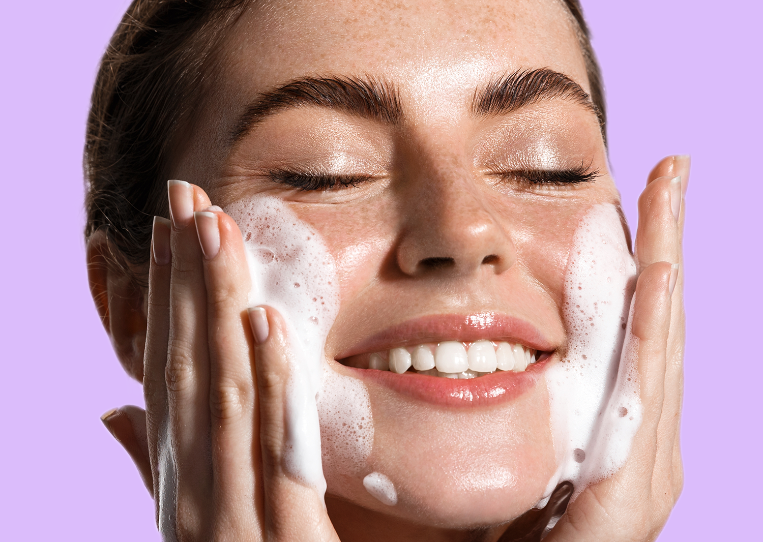Smiling woman washing her face with foaming cleanser, representing skincare tips for those in their 30s