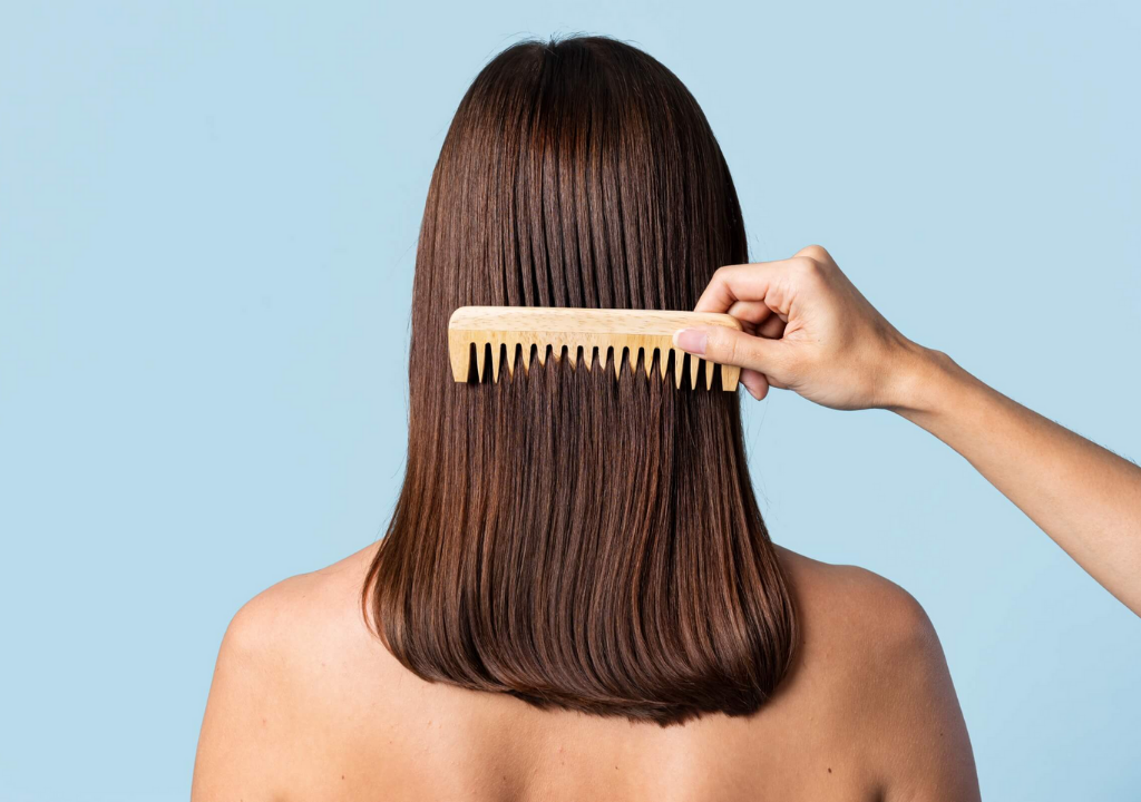Back view of a woman combing her sleek, brunette hair featuring an article covering rice water’s benefits for hair and how to make an at-home DIY treatment