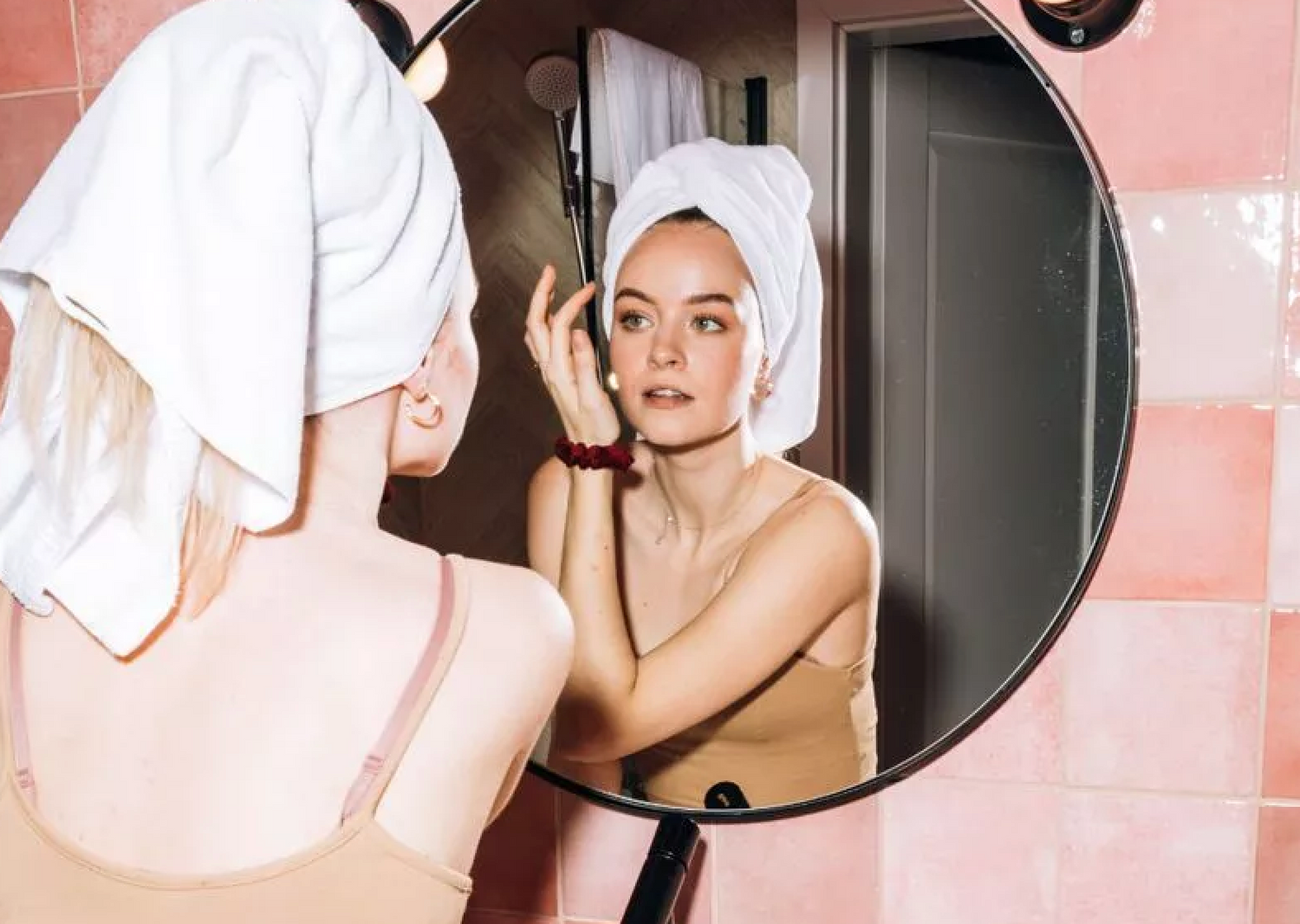 Woman in a towel looking in the mirror, explaining 10 reasons for puffy face causes and solutions by Dr. Idriss