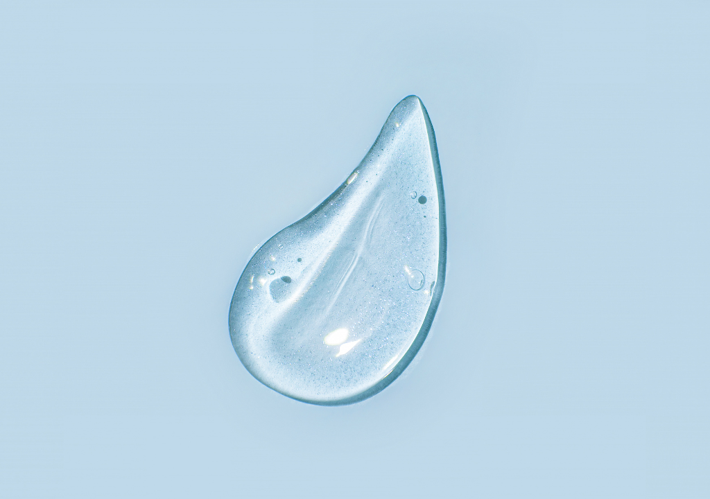 Close-up of a clear gel droplet on a blue background, representing the hydrating benefits of panthenol for skin and hair