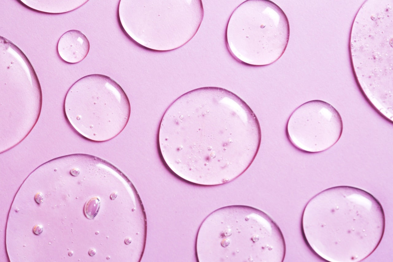 Close-up of niacinamide serum drops on a pink background, illustrating the ingredients benefits in skin care