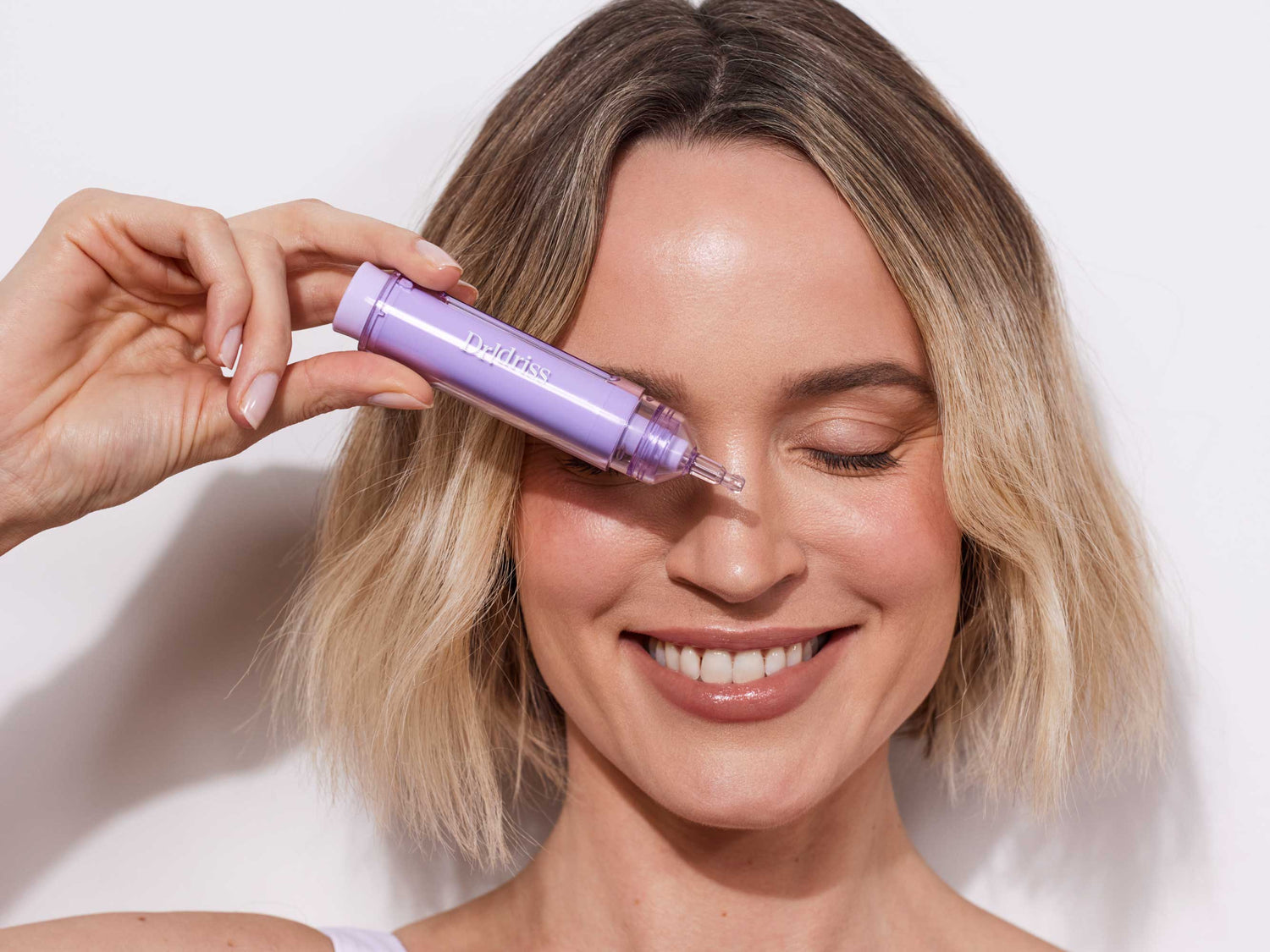 Smiling woman holding Dr. Idriss Hyper Serum near her face, highlighting its compatibility with retinol and benefits for uneven skin tone