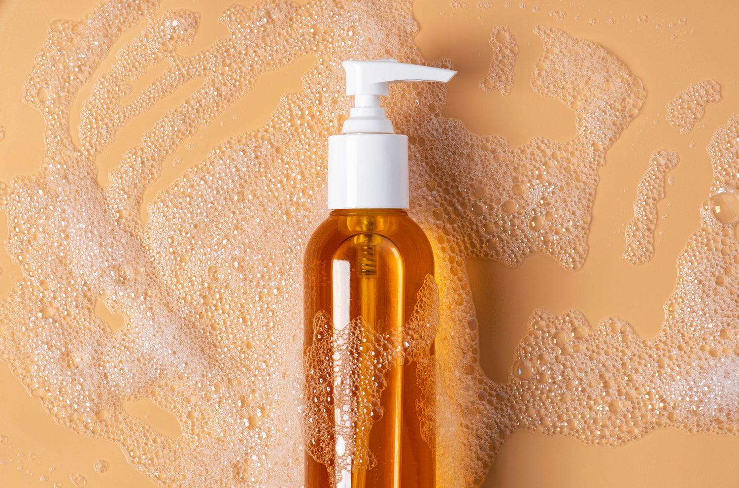 Amber-hued cleansing oil surrounded by bubbles against an orange background, emphasizing the importance of double cleansing