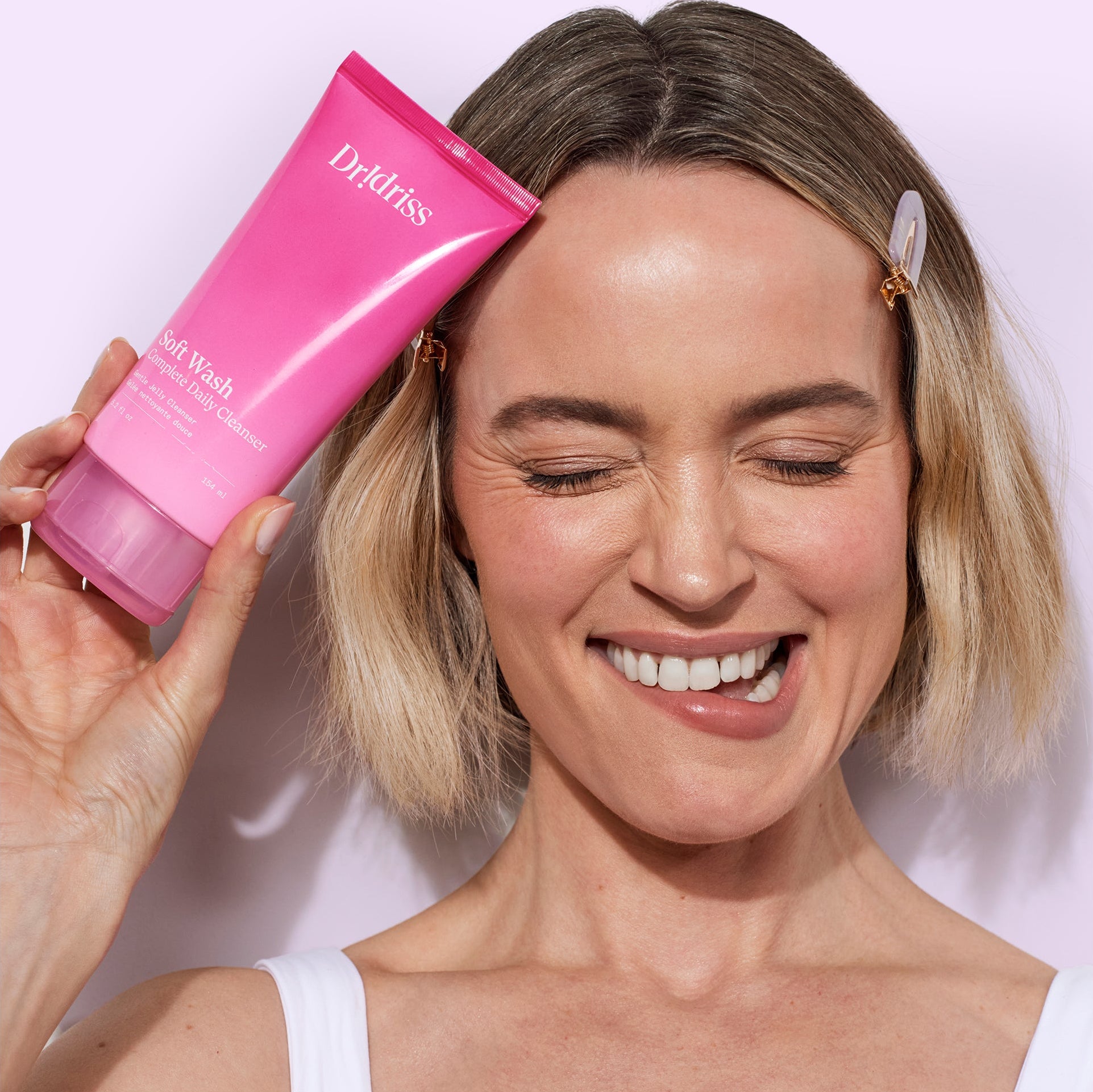 Woman holding Dr. Idriss Soft Wash tube smiling with glowing, clean skin