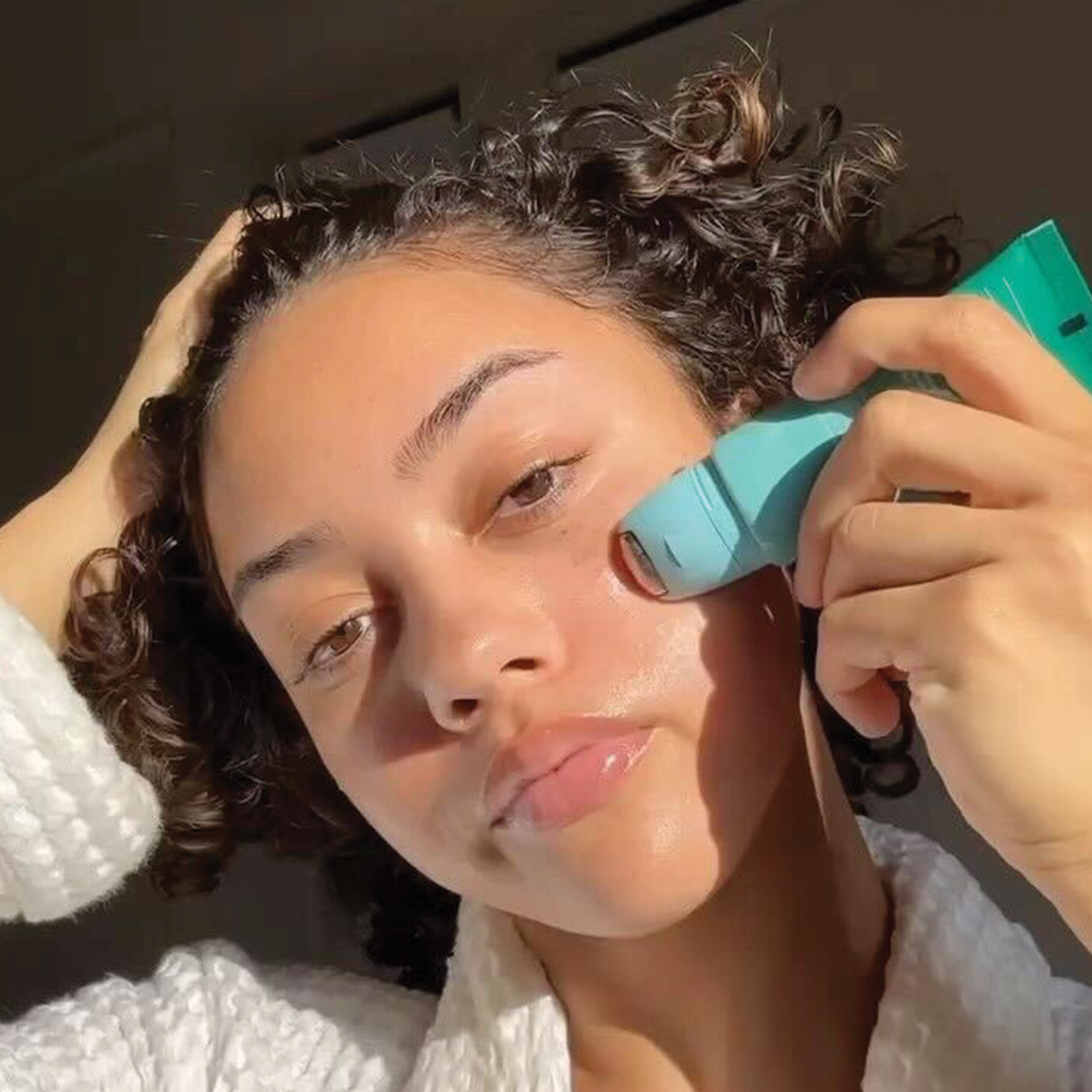 Close-up of woman rolling Dr. Idriss The Depuffer on dewy skin, showcasing a radiant, hydrated complexion