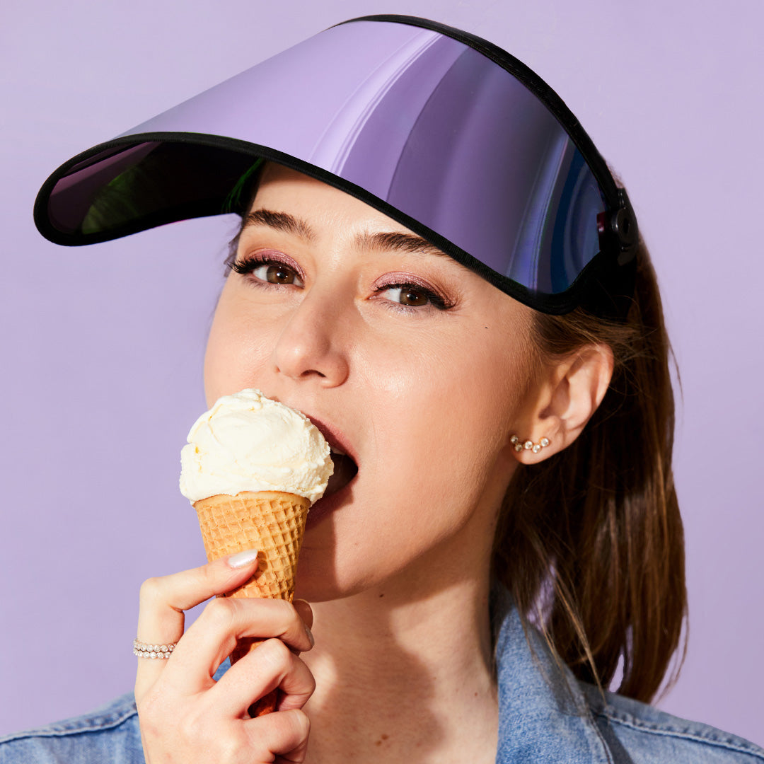 Dr. Shereene Idriss wearing a lilac UPF sun visor, eating an ice cream cone, against a lilac background