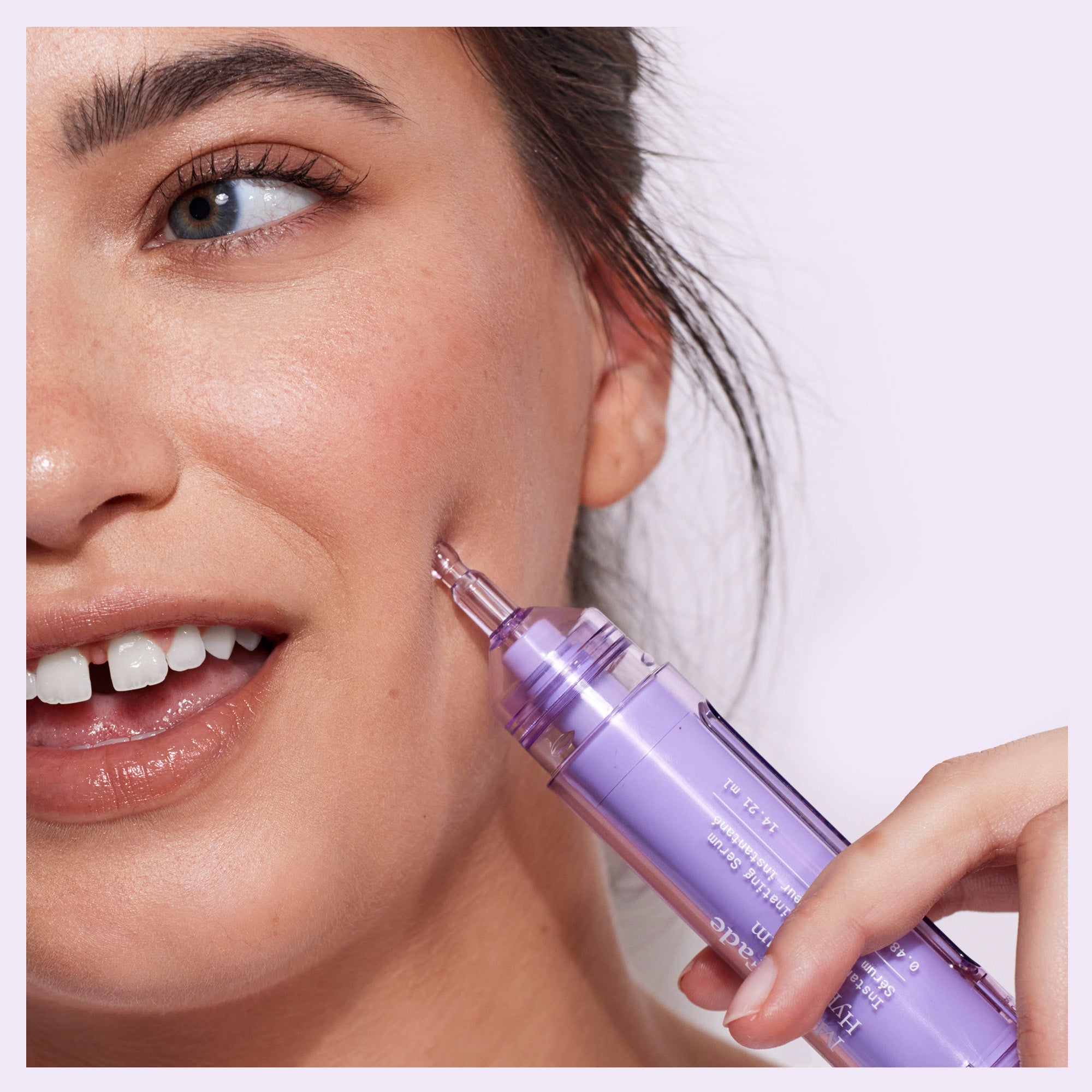Smiling woman applying Dr. Idriss Hyper Serum to her cheek, showcasing healthy, glowing skin and the product's syringe-like applicator
