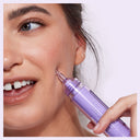 Smiling woman applying Dr. Idriss Hyper Serum to her cheek, showcasing healthy, glowing skin and the product's syringe-like applicator