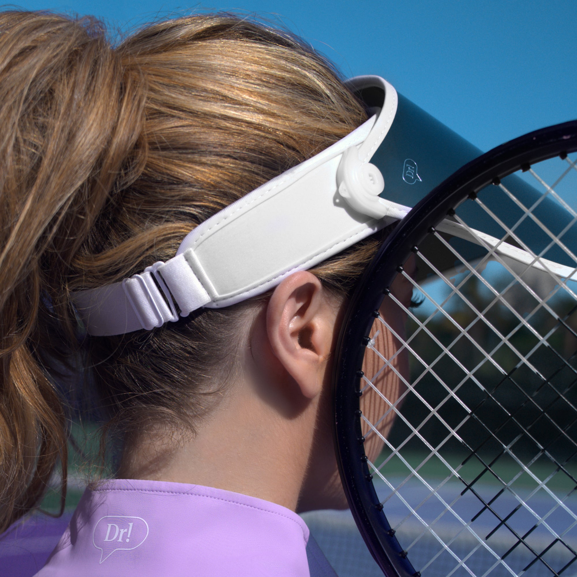 Dr. Shereene Idriss wearing the Major Shade Full Lux Sunshield in White with a tennis racket next to her face, showing the back of the visor in the new White color