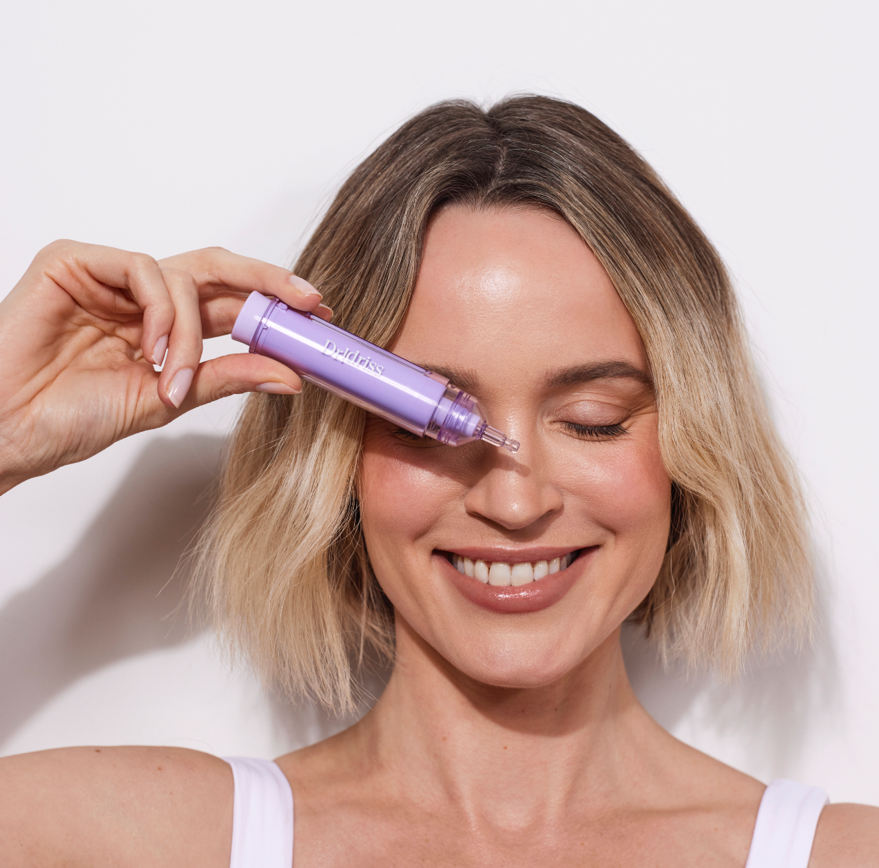Woman holding Dr. Idriss Major Fade Hyper Serum against her eye, smiling with radiant skin against a clean, white background